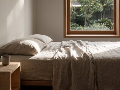 Dormitorio sereno con luz natural entrando por una ventana de madera y ropa de cama de lino